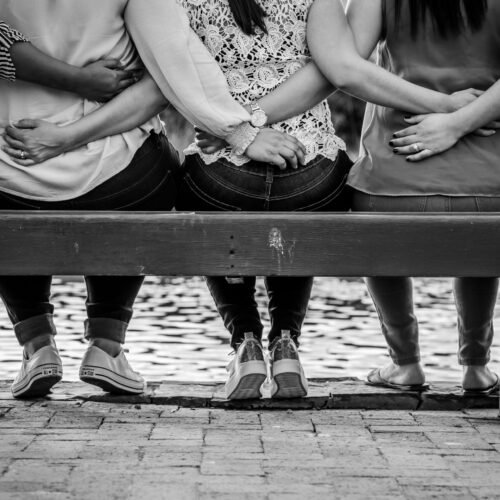 grayscale photo of 3 women sitting on wooden bench